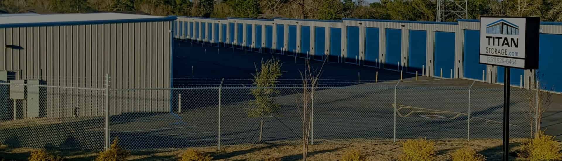 Entrance view of Titan Storage - Spanish Fort showing high fencing with barbed wire, gate, and some unit doors and drive